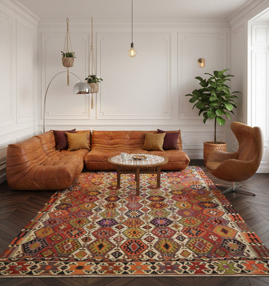 Très grand tapis de salon en laine Aydin aux motifs géométriques multicolores (365 x 220 cm) mis en situation avec un canapé modulaire en cuir cognac, un fauteuil Egg et des murs blancs à moulures classiques