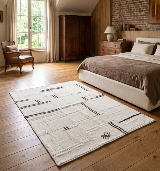 Kilim patchwork en chanvre, tapis contemporain tissé main à partir de kilims anciens d'Anatolie recomposés, motif rayé écru et brun posé dans une chambre en Normandie au mur de brique et mobilier ancien