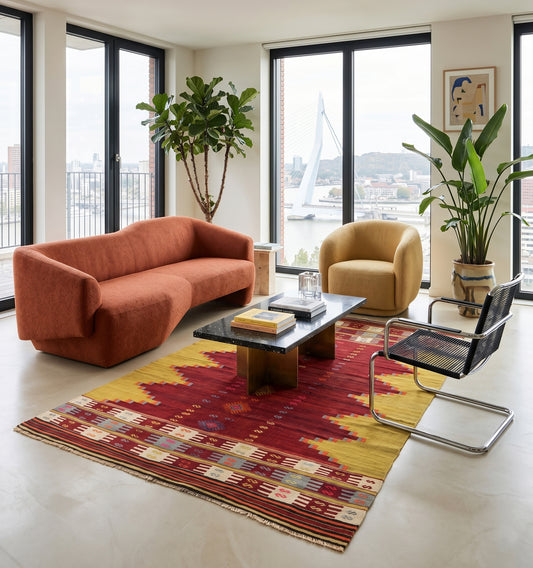 Tapis kilim Balikesir vintage de 65 ans aux teintes rouge et ocre, tissé à la main en Anatolie. Cette pièce d'artisanat d'exception sublime un loft moderne à Rotterdam, créant un contraste chic entre le tissage traditionnel, un mobilier aux lignes organiques et une vue urbaine lumineuse.