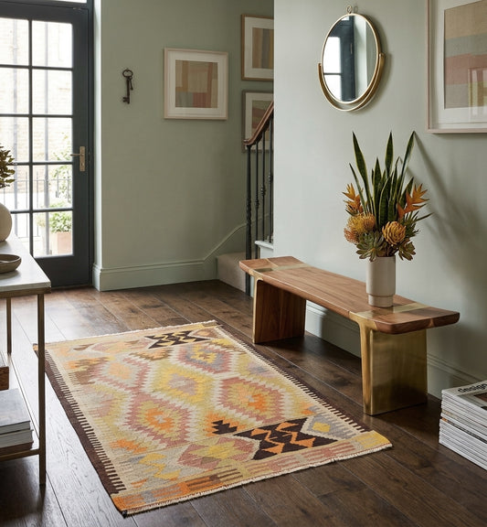 Tapis Kilim jaune et pastel 156x107 cm en laine dans une entrée lumineuse avec banc en bois design et parquet foncé.
