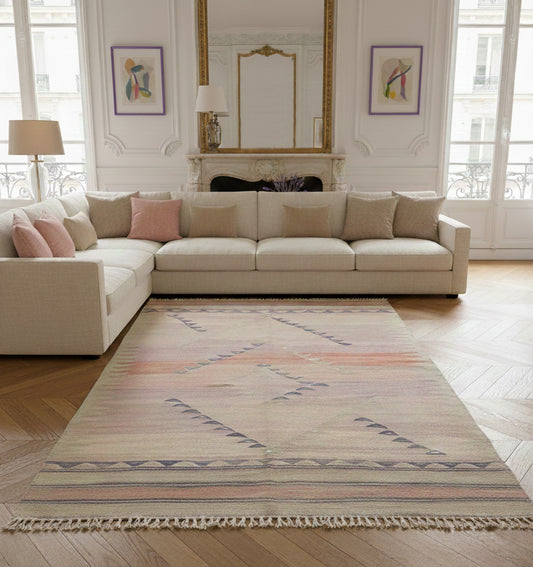 Grand tapis de salon en laine aux tons rose pastel et motifs géométriques gris (210 x 144 cm) mis en situation dans un salon lumineux avec canapé d'angle crème et parquet en chevrons