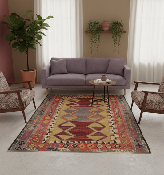 Tapis de salon en laine Obruk aux motifs géométriques rouge, jaune et gris (185 x 145 cm) mis en situation avec un canapé mauve, deux fauteuils vintage à motifs, des plantes vertes et des murs clairs