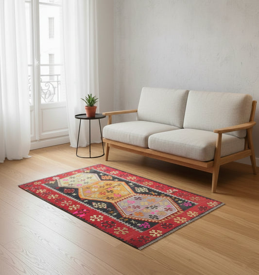 Petit tapis de salon en laine rouge aux motifs ethniques colorés (110 x 80 cm) mis en situation devant un canapé deux places en bois clair et tissu blanc