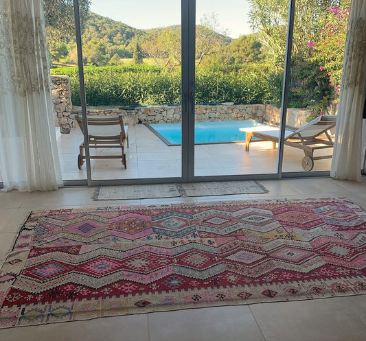Kilim Adana ancien 180x300 cm posé dans un salon à Ibiza, devant des baies vitrées donnant sur une piscine et des collines