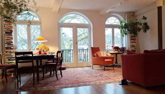 Grand tapis Kilim ancien Adana de 380x260 cm dans un salon lumineux à Anvers avec fauteuils rouges, bibliothèque et grandes baies vitrées.