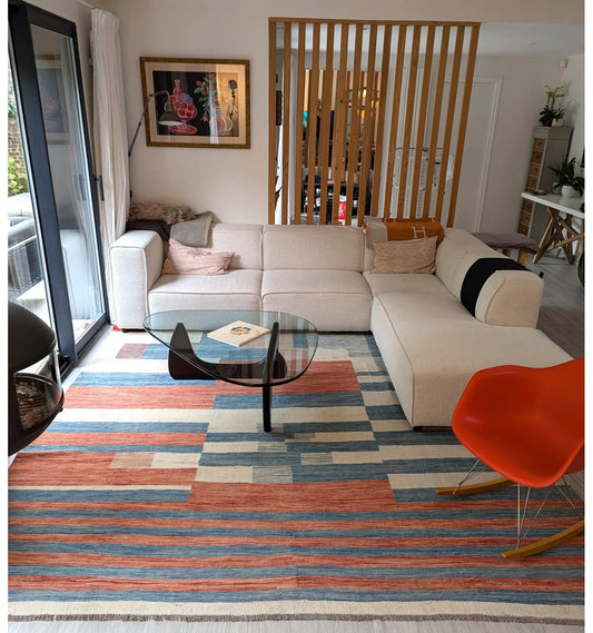 Grand tapis Kilim Art Déco bleu et orange de 350x250 cm sous un canapé d'angle blanc dans un salon moderne avec verrière à Sao Paulo.
