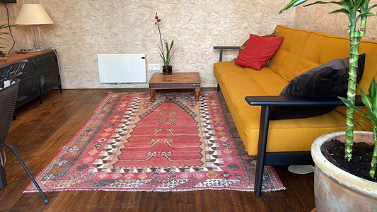 Kilim ancien Obruk Konya 200x148 cm dans un salon d'Amsterdam, posé sur parquet sombre devant un canapé moutarde, mur en pierre brute
