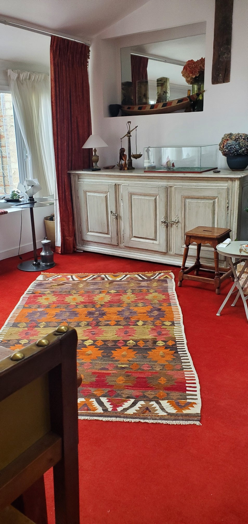 Kilim ancien Nigde 211x133 cm posé en biais sur une moquette rouge dans un salon parisien du 7e arrondissement, motifs étoiles orange, rouge et ocre
