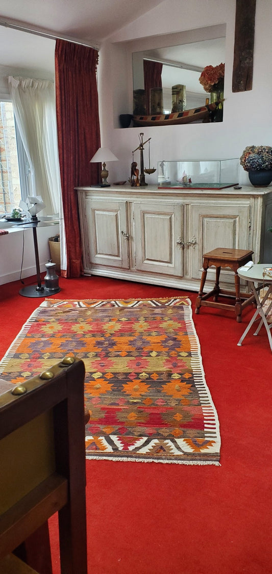 Kilim ancien Nigde 211x133 cm posé en biais sur une moquette rouge dans un salon parisien du 7e arrondissement, motifs étoiles orange, rouge et ocre