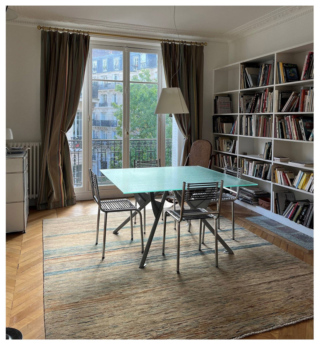 Tapis noué Art Déco 300x250 cm dans une salle à manger à Paris 19ème, table en verre, chaises métal, bibliothèque blanche, parquet en point de Hongrie