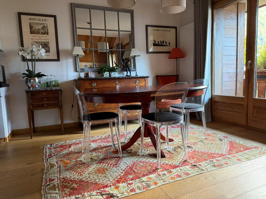 Salle à manger de caractère avec tapis kilim ancien d'Anatolie, table ovale en bois massif et chaises transparentes contemporaines.