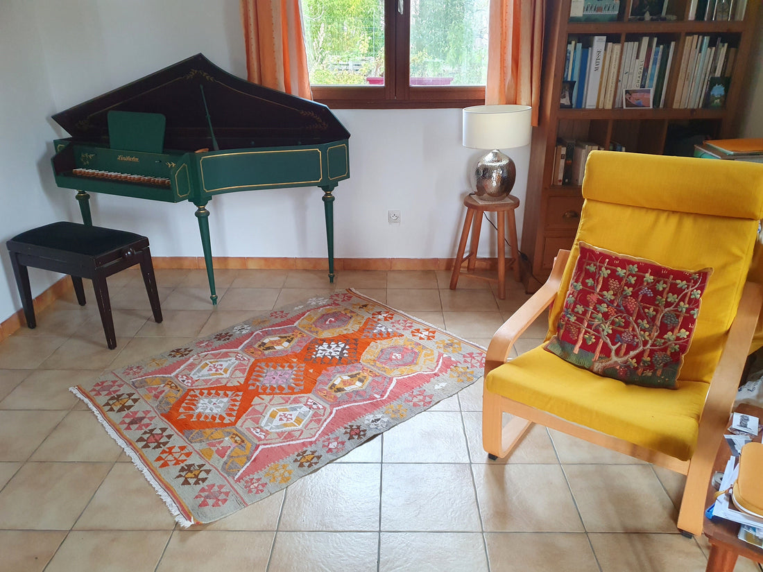 Kilim ancien Adana 148x118 cm posé dans un salon à Bordeaux, clavecin vert et fauteuil jaune en arrière-plan, carrelage clair
