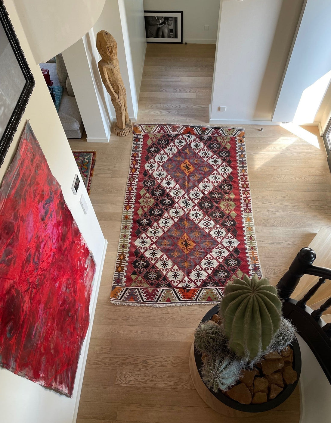 Kilim ancien Adana 292x166 cm photographié en plongée dans un couloir à Bruxelles, parquet clair, toile rouge, cactus en pot