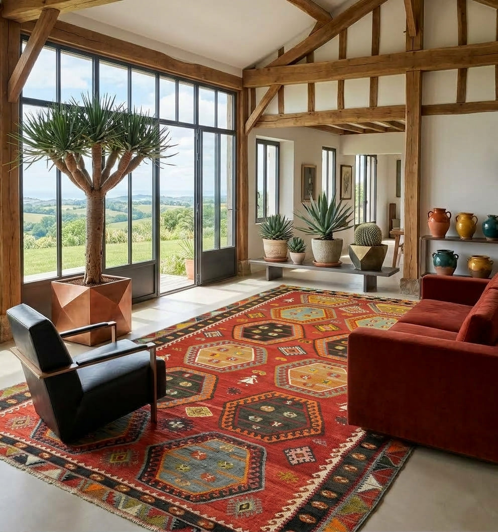 Grand Kilim d'Anatolie aux motifs hexagonaux rouges et bleus, ancrant un salon de luxe baigné de lumière sous une verrière, avec charpente apparente et mobilier contemporain élégant.