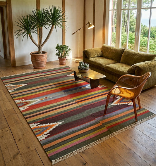 Grand tapis Kilim aux rayures horizontales multicolores et motifs ethniques, structurant un salon lumineux avec canapé en velours olive, chaise design translucide et parquet en chêne massif.