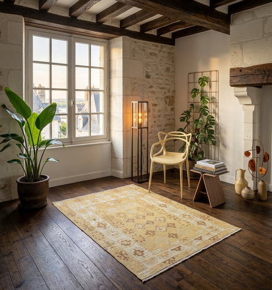 Kilim d'Anatolie aux teintes ocre et sable, tissage artisanal en laine illuminant une pièce de caractère aux murs en pierre et poutres apparentes, marié à une chaise design et un parquet sombre.