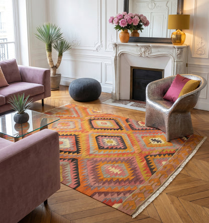 Kilim ancien de Barak, Anatolie, grands motifs géométriques orange, rose et ocre tissé main en laine naturelle, dans un salon avec cheminée en marbre à Lyon.