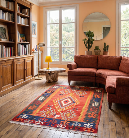 Kilim ancien Cal, tapis kilim tissé main en laine par des nomades d'Anatolie, médaillon central et bordure de motifs colorés, posé dans un salon bibliothèque parisien face aux balcons en fer forgé