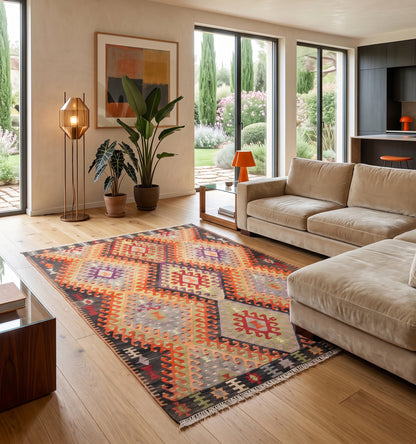 Kilim ancien Cal, tapis kilim tissé main en laine par des nomades d'Anatolie, losanges rouge et prune sur fond graphique, posé dans un salon en Provence face aux cyprès et au jardin fleuri