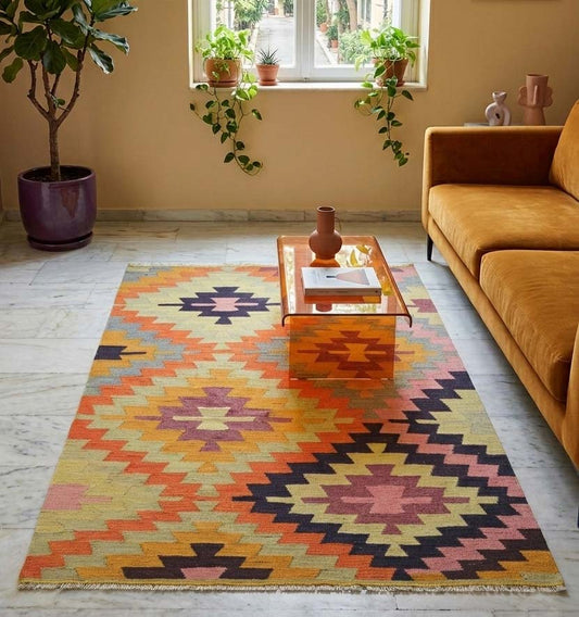 Tapis Kilim authentique aux motifs géométriques vibrants, orange, jaune et pourpre, tissé main, réchauffant un salon minimaliste au mobilier moderne, canapé en velours et table en verre, posé sur sol en marbre lumineux.