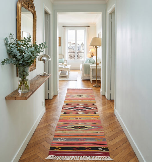 Kilim tribal de Denizli aux motifs géométriques multicolores tissé main en laine d'Anatolie, déroulé dans un couloir épuré aux murs blancs et parquet point de Hongrie à Bordeaux.