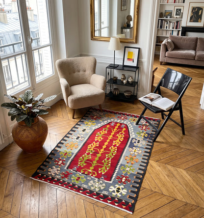 Kilim ancien d'Esme, tapis kilim tissé main en laine par des nomades d'Anatolie, médaillon rouge à motif d'arbre de vie, posé sur parquet en chevrons dans un appartement parisien face aux toits de zinc