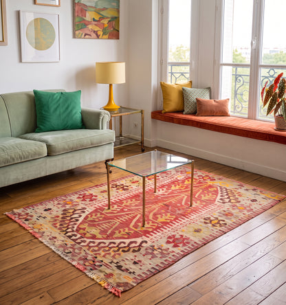Kilim ancien d'Esme, tapis kilim tissé main en laine par des nomades d'Anatolie, motif floral central rouge et safran, posé dans un salon parisien près d'une banquette sous fenêtre à balcon