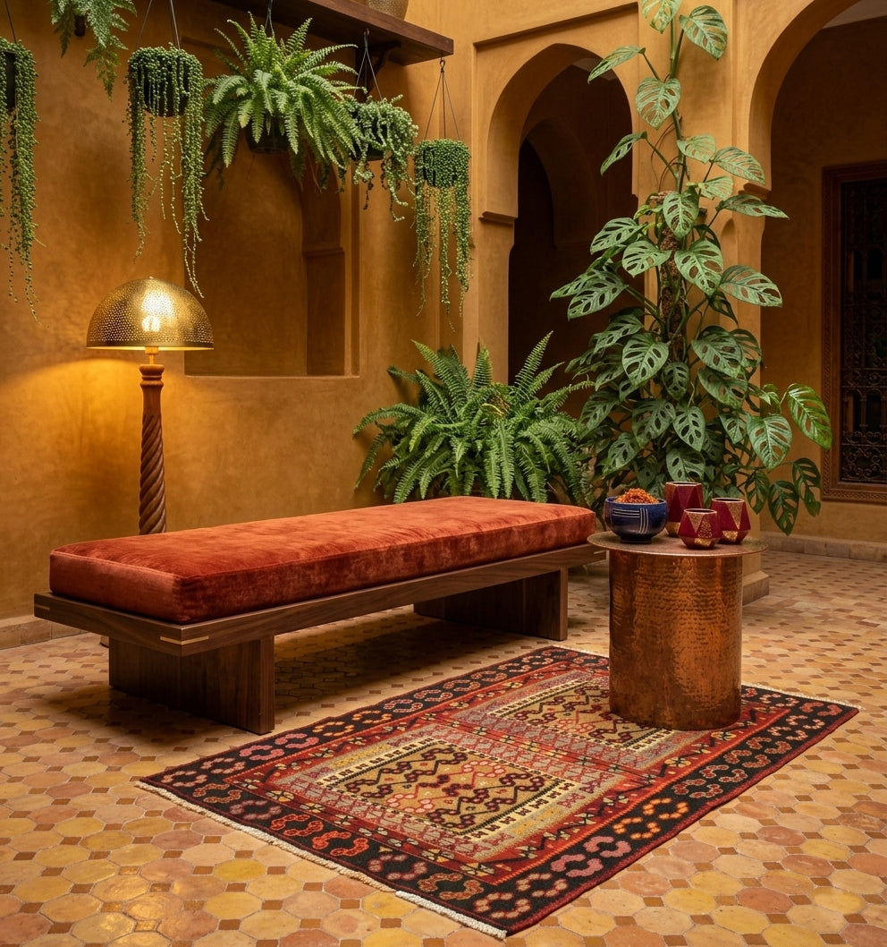 Tapis Kilim Kayserie vintage en laine aux motifs rouges et noirs étendu sur un sol en zelliges dans un riad marocain traditionnel avec patio arboré