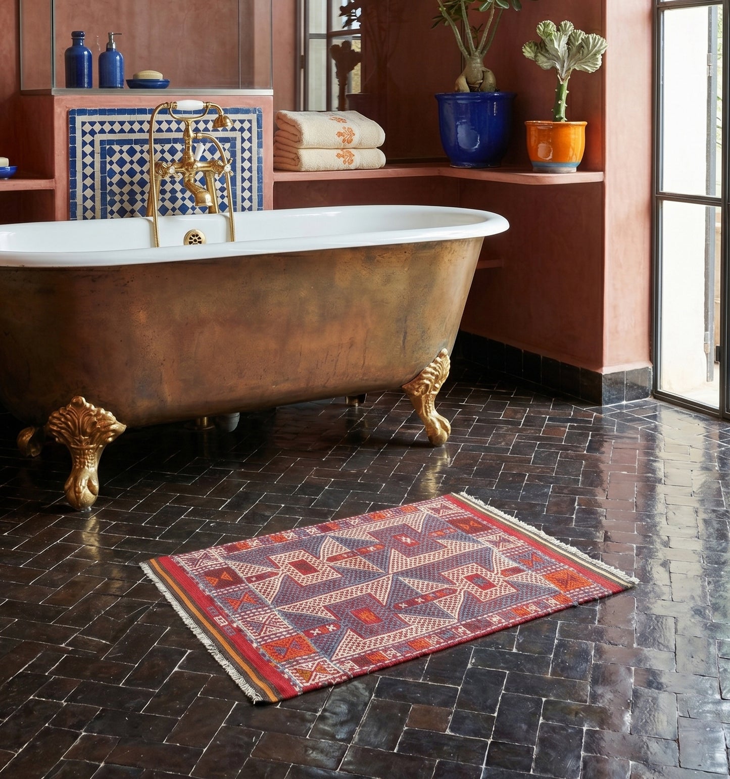 Kilim ancien de Kozak, Anatolie, motifs géométriques bleu, rouge et crème tissé main en laine naturelle, devant une baignoire dorée dans un riad à Marrakech.