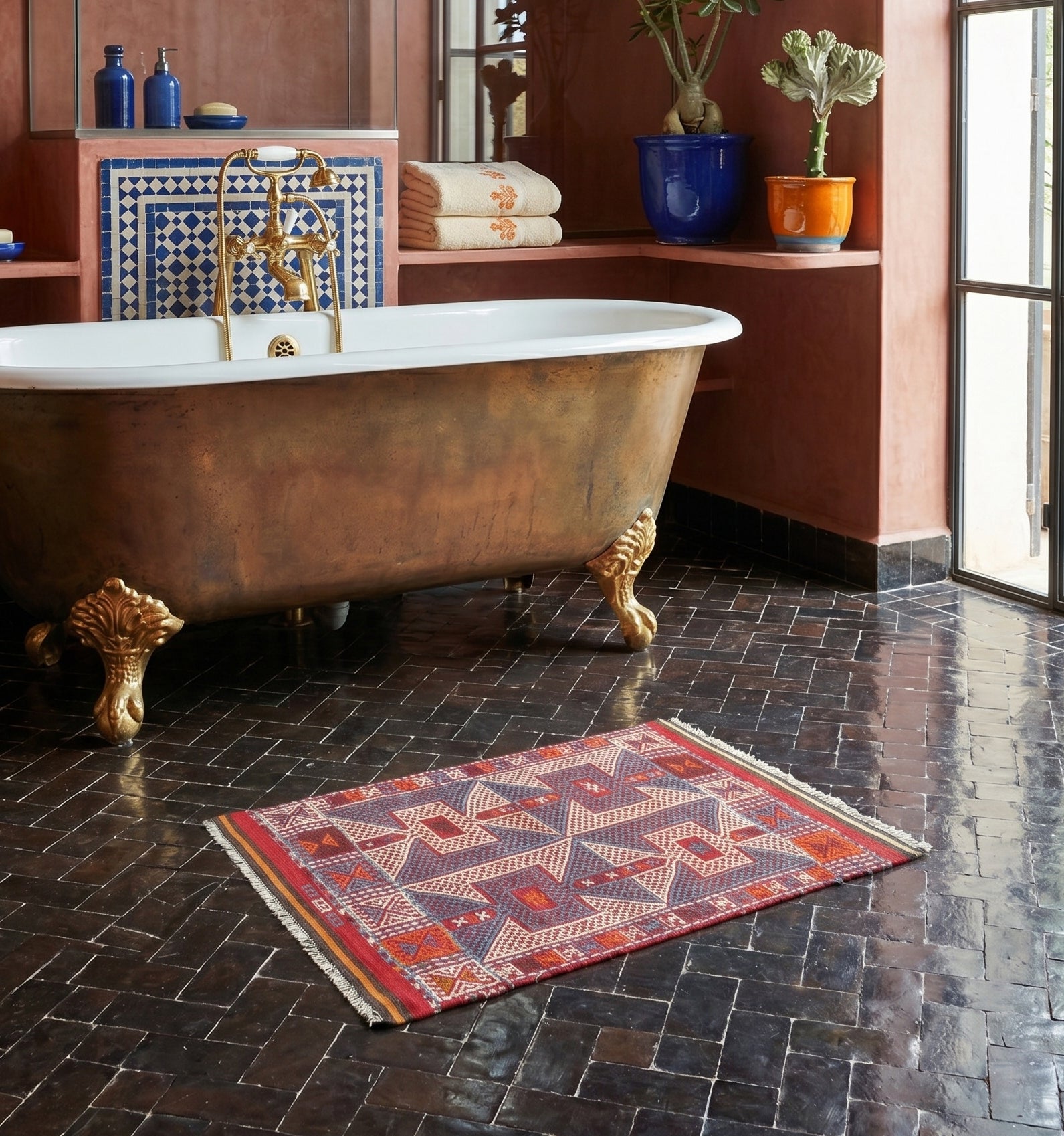 Kilim ancien de Kozak, Anatolie, motifs géométriques bleu, rouge et crème tissé main en laine naturelle, devant une baignoire dorée dans un riad à Marrakech.