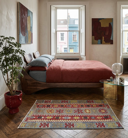 Tapis Kilim multicolore 140x84 cm en laine posé sur un parquet en chevrons dans une chambre design avec lit en bois et linge de lit terre de Sienne.