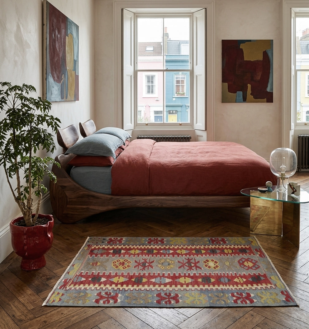 Tapis Kilim multicolore 140x84 cm en laine posé sur un parquet en chevrons dans une chambre design avec lit en bois et linge de lit terre de Sienne.