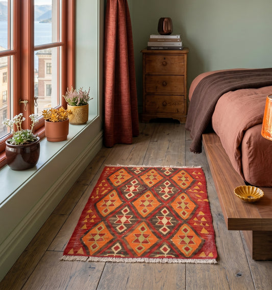 Kilim ancien de Sivas, Anatolie, motifs géométriques orange, rouge et brun tissé main en laine naturelle, en descente de lit dans une chambre cosy à Oslo.