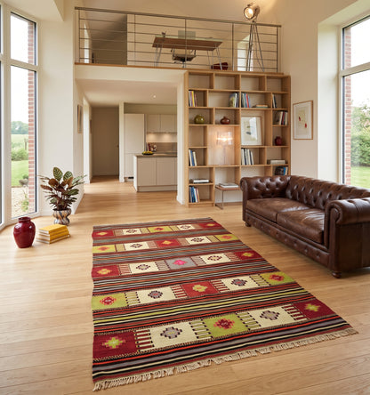 Tapis kilim Balikesir en laine aux rayures horizontales et motifs géométriques colorés (260 x 145 cm) mis en situation dans un salon moderne avec canapé en cuir, grandes baies vitrées donnant sur un jardin près de lLille, plantes exotiques et blibliothèque moderne.