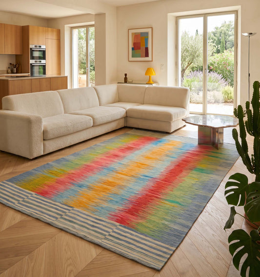 Tapis kilim contemporain d'Anatolie aux rayures vibrantes multicolores (bleu, jaune, rouge), tissé main, réchauffant un salon chic et lumineux. L'artisanat ancien du kilim contraste élégamment avec le mobilier moderneet une baie vitrée panoramique donnant sur un paysage de jardin en Provence. Signé Anatolie Kilim.