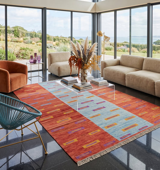 Kilim tissé main aux motifs géométriques rythmés sur fond bicolore corail et bleu, tapis kilim contemporain d'inspiration Anatolie posé dans une villa en Bretagne face à l'océan, pièce unique aux lignes vives