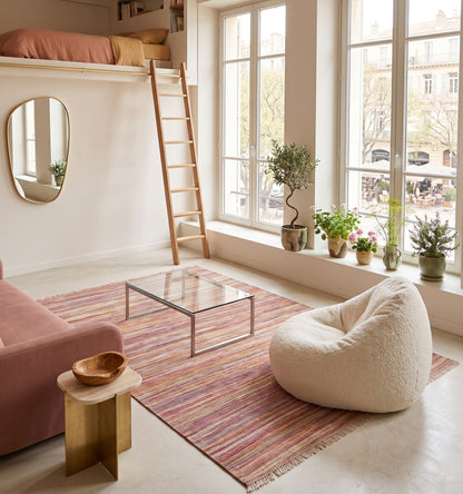 Kilim tissé main aux nuances chinées rose et corail, tapis kilim contemporain d'inspiration Anatolie posé sous une mezzanine à Marseille face à une place ensoleillée, pièce unique dans un intérieur baigné de lumière