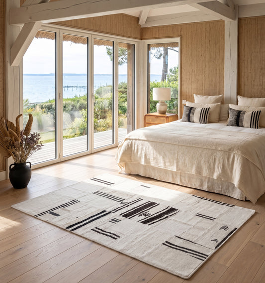 Kilim patchwork en chanvre, tapis contemporain tissé main à partir de kilims anciens d'Anatolie recomposés, motif rayé noir et écru posé face à la vue mer du bassin d'Arcachon, chambre en bois clair esprit cabane