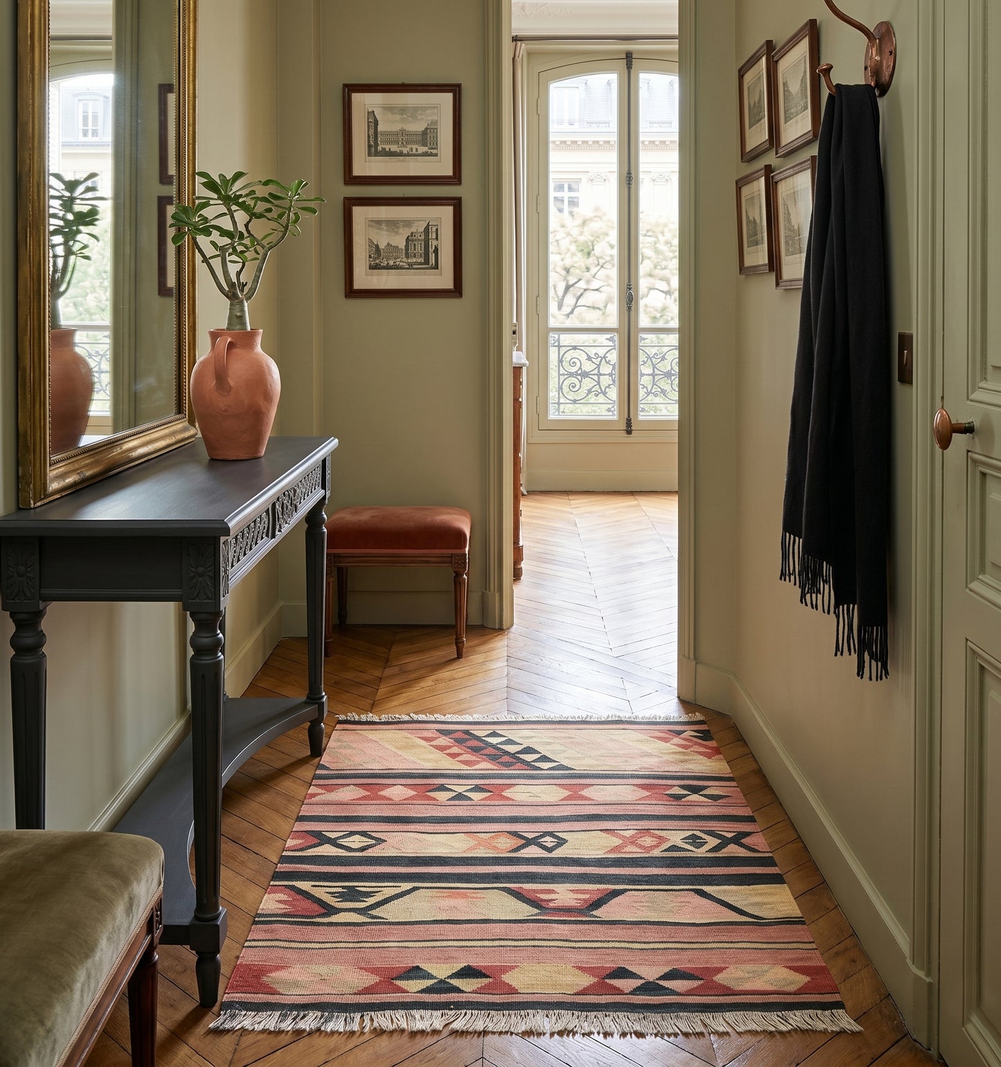 Tapis kilim ancien d'Anatolie aux motifs géométriques noirs et rosés, accueillant les visiteurs dans l'entrée élégante d'un appartement de style à Nantes. Un tissage artisanal unique qui sublime une console sombre et un miroir doré pour une ambiance chic et chaleureuse.