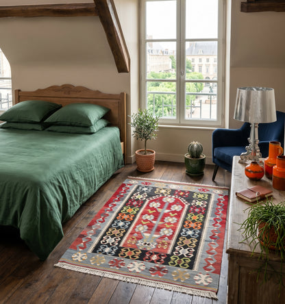 Petit tapis kilim ancien Esmé (130 x 96 cm) aux riches motifs géométriques et losanges rouges, blancs et bleus, réchauffant un parquet ancien dans un intérieur raffiné à Reims. Ce tissage d'Anatolie de 60 ans d'âge apporte une touche d'artisanat unique et authentique à une décoration moderne.