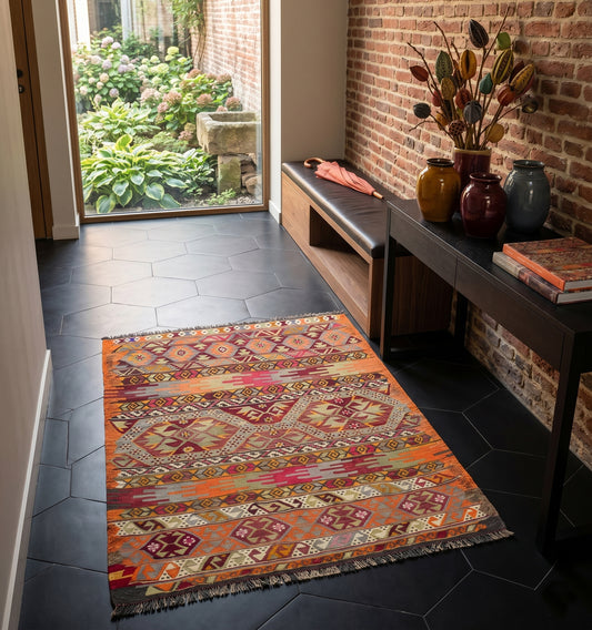 Petit tapis kilim ancien Menemenci (110 x 95 cm) aux motifs géométriques noirs et écrus, disposé devant un fauteuil moderne dans un intérieur à Strasbourg. Un tissage artisanal d'Anatolie de 65 ans d'âge qui apporte un caractère authentique et chic à la décoration.