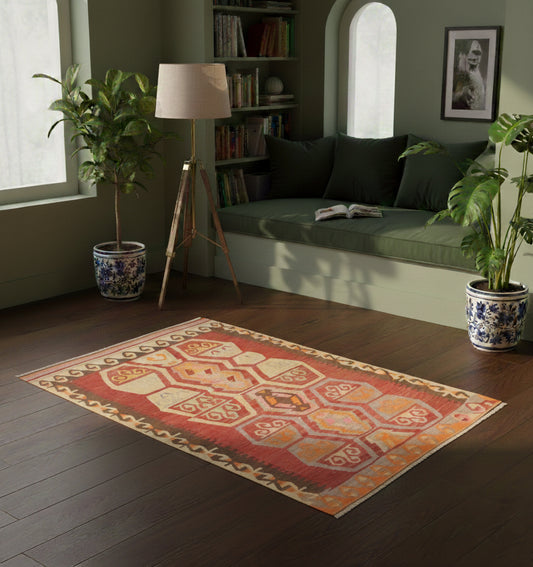 Petit tapis en laine Adana aux motifs d'hexagones ocre et terre cuite (115 x 90 cm) mis en situation dans un coin lecture apaisant avec banquette intégrée vert sauge, coussins assortis, plantes vertes et lumière naturelle