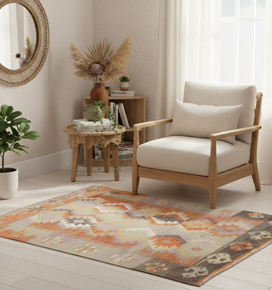 Tapis de chambre en laine Adana aux motifs géométriques gris, orange et ocre (160 x 124 cm) mis en situation avec un fauteuil en bois clair, un miroir soleil en rotin et des murs de couleur crème.