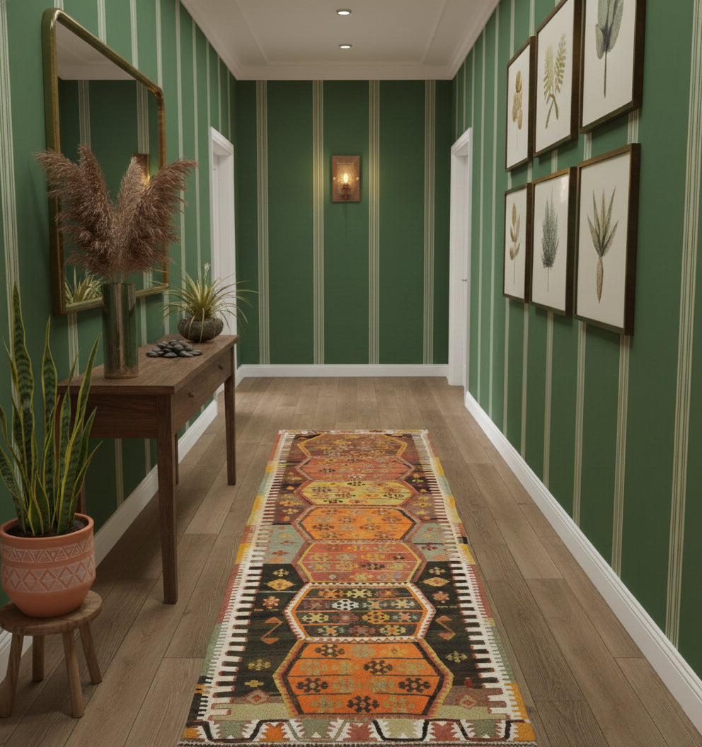 Long tapis d'entrée ou de couloir en laine aux motifs géométriques orange et noir (330 x 96 cm) mis en situation dans un couloir aux murs verts avec une console en bois