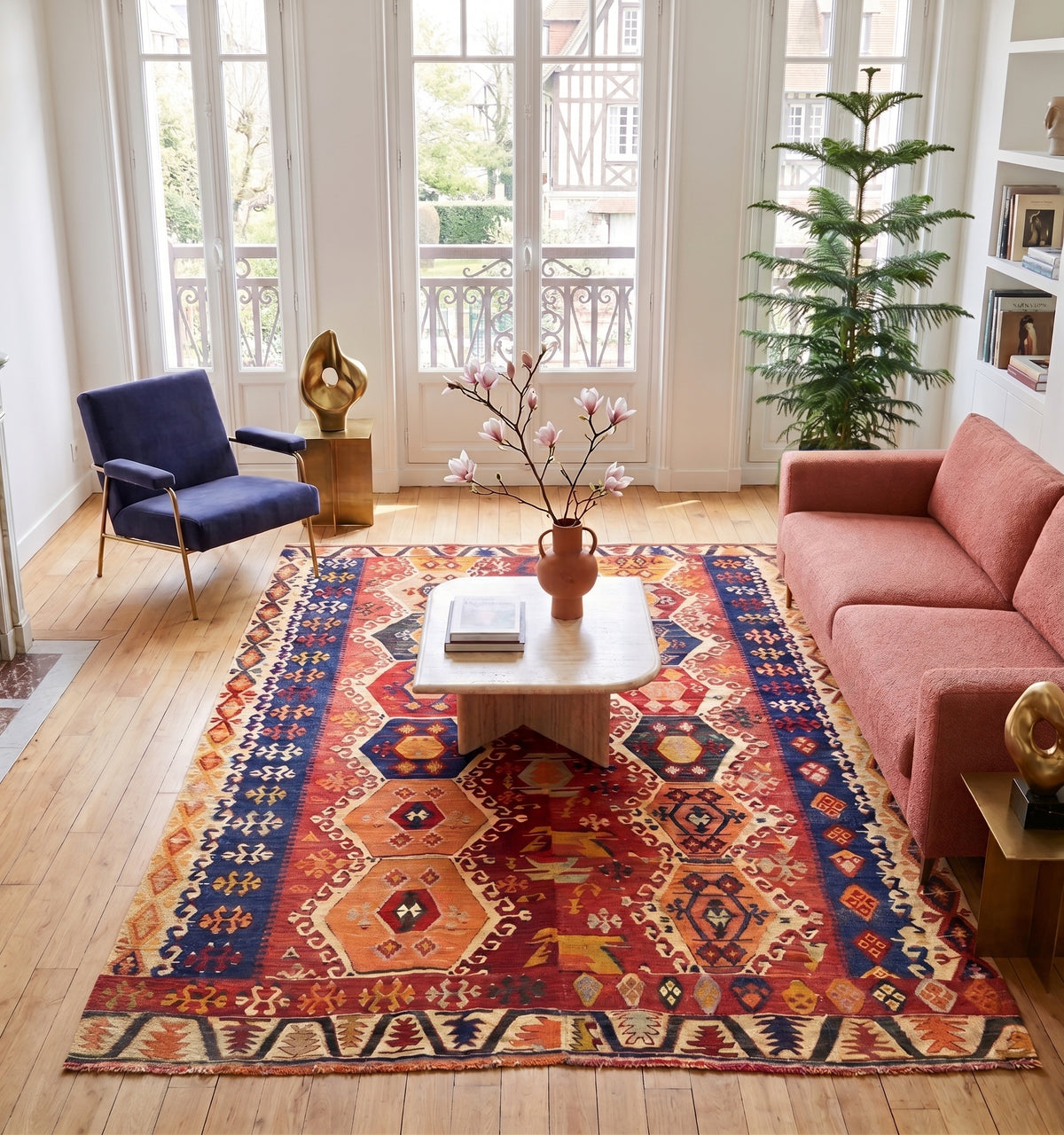Tapis kilim ancien d'Adana, tissé main en laine par des nomades d'Anatolie, médaillons hexagonaux rouge et orange sur bordure bleu nuit, posé dans un salon à Deauville face à une maison à colombages et un balcon en fer forgé