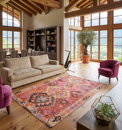 Tapis kilim ancien d'Adana, tissé main en laine par des nomades d'Anatolie, médaillon rose poudré et corail patiné par le temps, posé dans un chalet à Megève sous charpente en bois face à la vue sur les montagnes