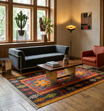 Kilim anatolien aux motifs tribaux audacieux sur fond gris anthracite et bordure rouge, créant un contraste saisissant dans un salon au design moderne avec canapé gris épuré et mobilier en laiton.