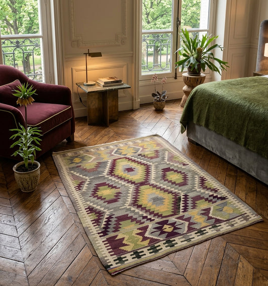 Tapis kilim ancien d'Anatolie en laine aux motifs de diamants pourpre et vert, marié à un fauteuil en velours bordeaux et un parquet en point de Hongrie dans un intérieur lyonnais raffiné.
