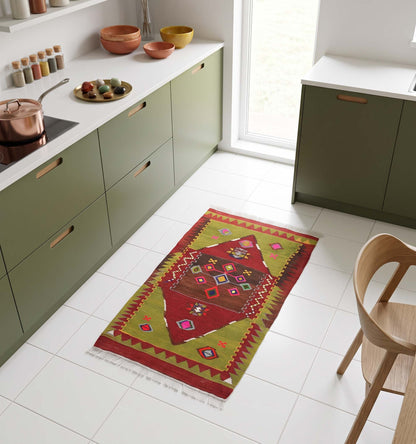 Tapis kilim ancien de Yozgat, tissé main en laine par des nomades d'Anatolie, médaillon losangé rouge et brun sur bordure dents de loup vert olive, posé dans une cuisine nantaise aux façades vert olive et carrelage blanc