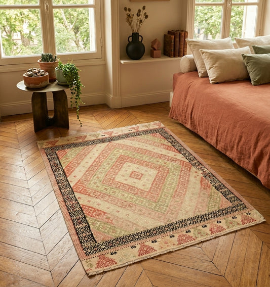 Tapis kilim d'Anatolie aux tons pastel et motifs losanges, disposé sur un parquet en point de Hongrie dans une chambre parisienne chic au style haussmannien.